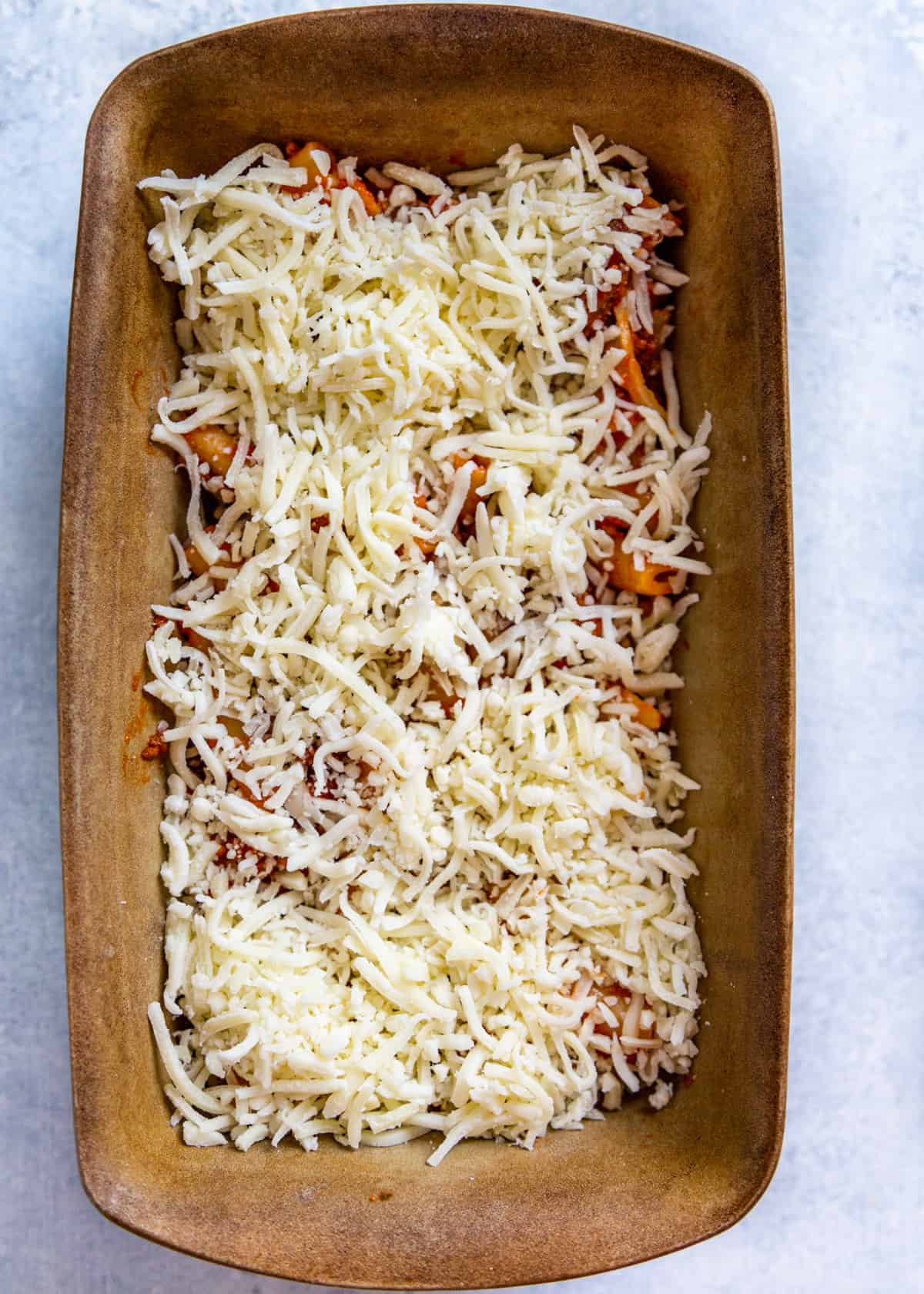 overhead: ziti and sauce covered in cheese in a baking dish