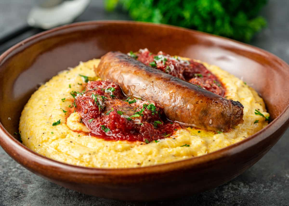 side view: Italian sausage ragu over creamy polenta in a brown ceramic bowl