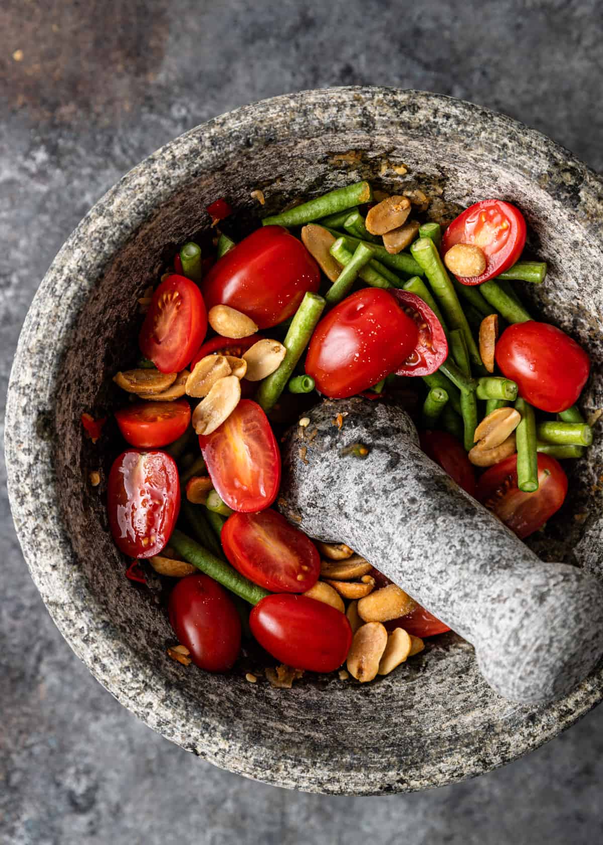 overhead: adding green beans, tomatoes, and peanuts to mortar and pestle