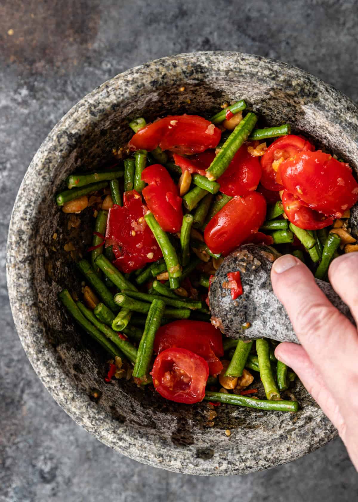 overhead: mashing green beans, tomatoes, and peanuts with mortar and pestle