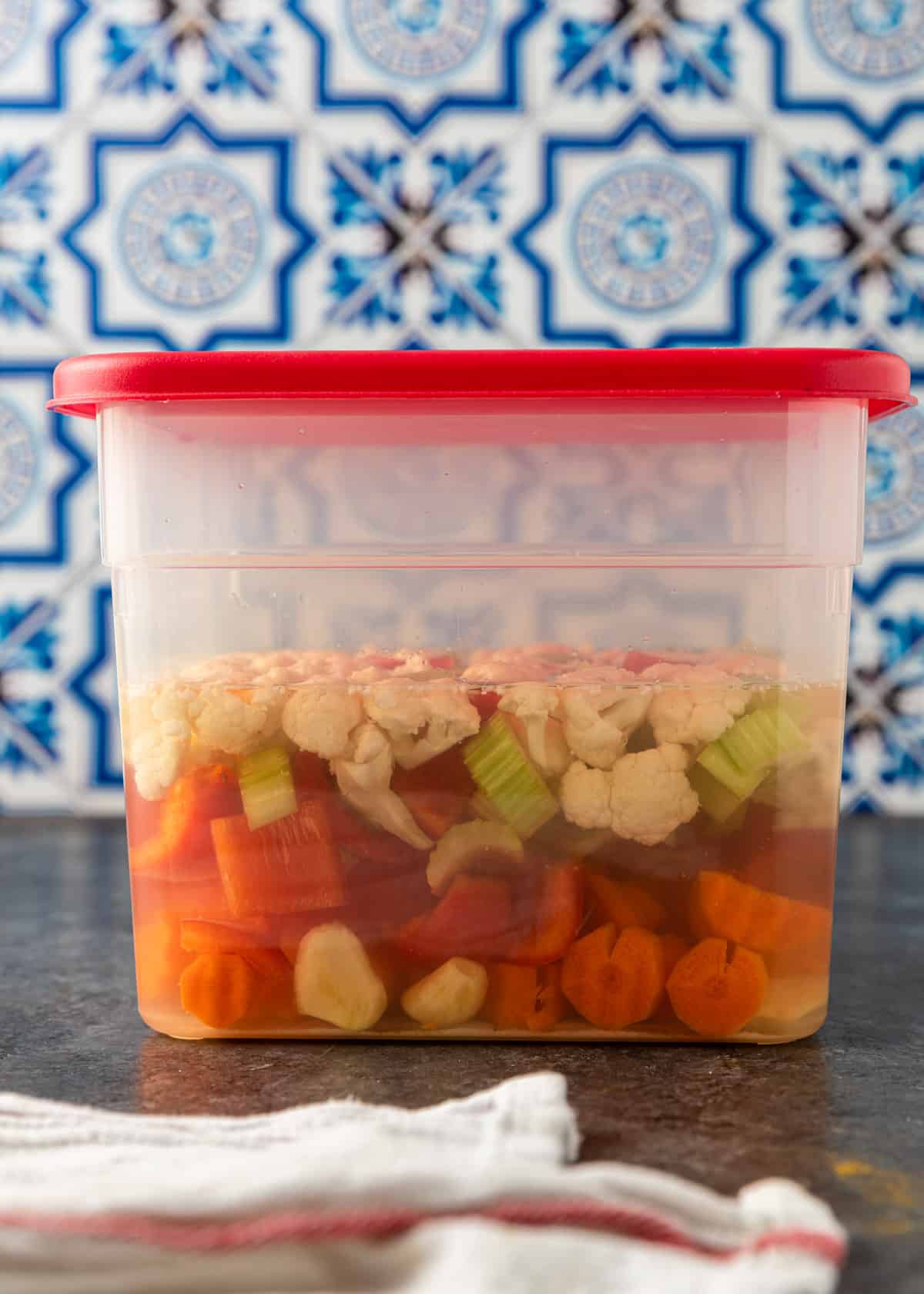 salting the vegetables in salt water in a clear container with a red lid
