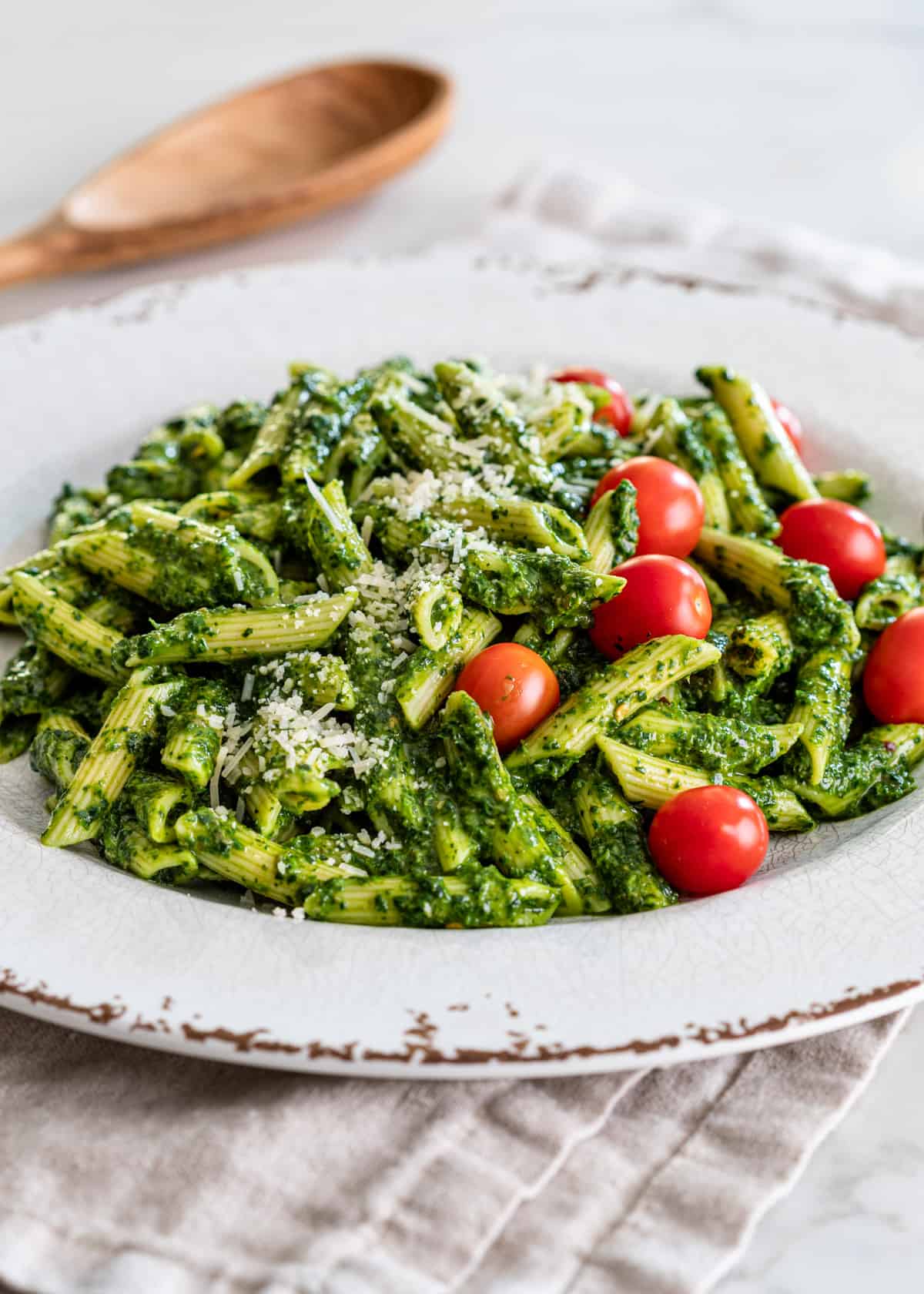 penne with sauce verde in a white plate with grated cheese and cherry tomatoes on top