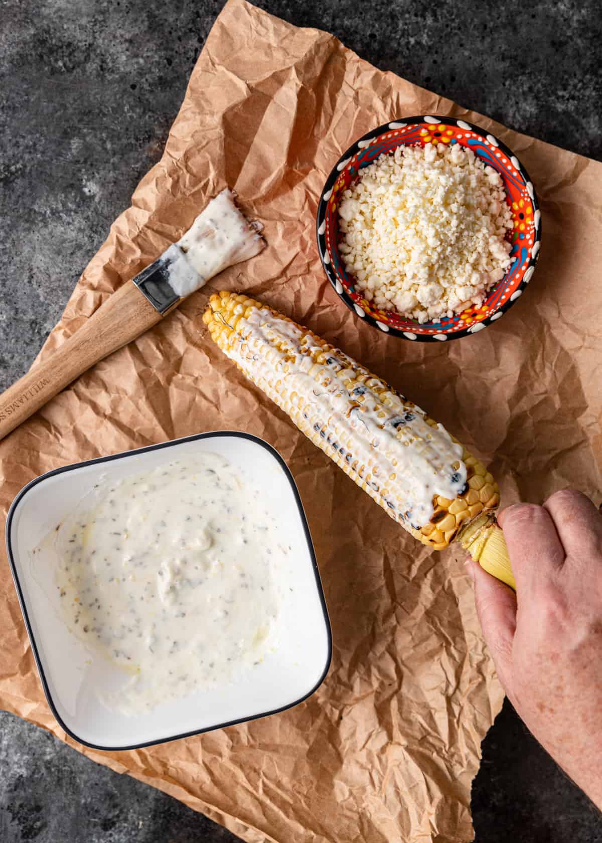 overhead: brushing grilled corn on the cob with yogurt sauce and feta