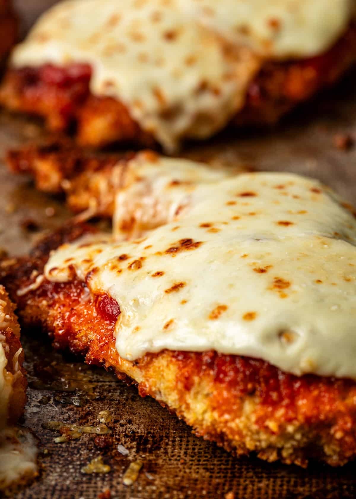 extreme closeup: baked chicken parmigiana on a baking sheet covered in melted cheese
