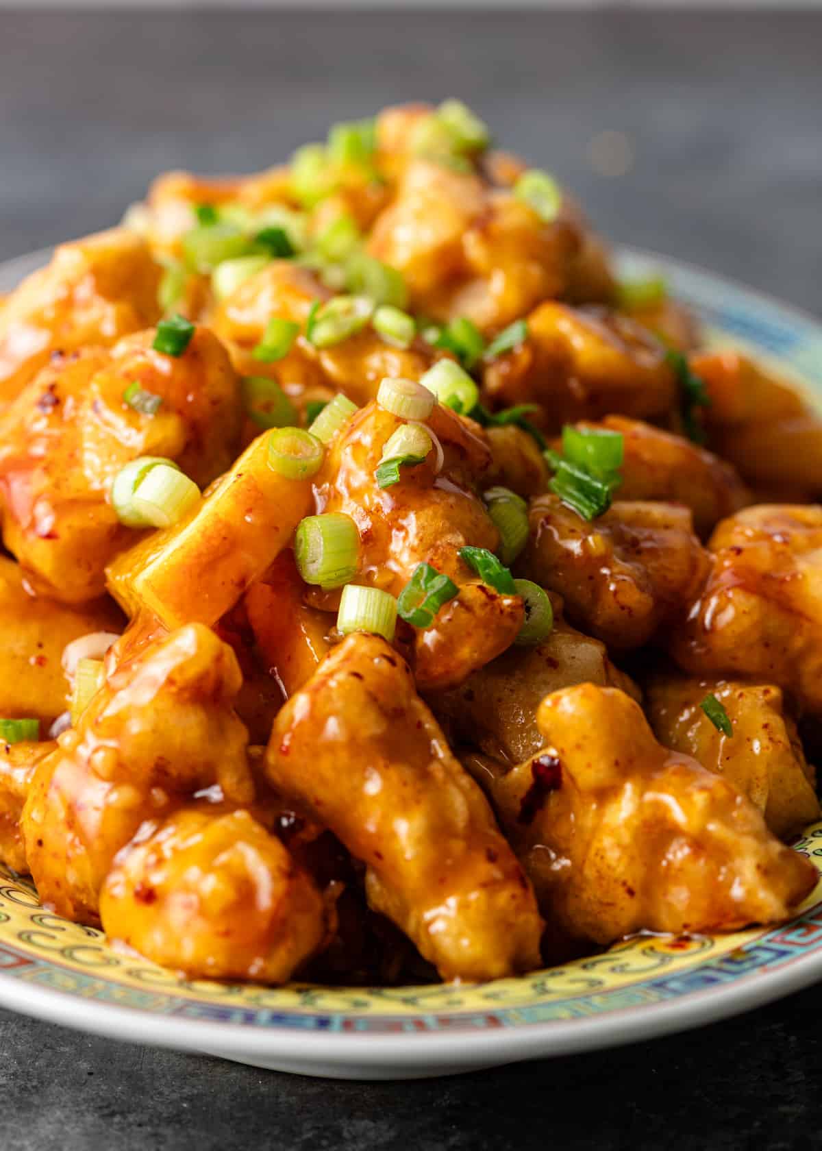 closeup: a heaping pile of orange chicken with sticky sauce and sliced green onions