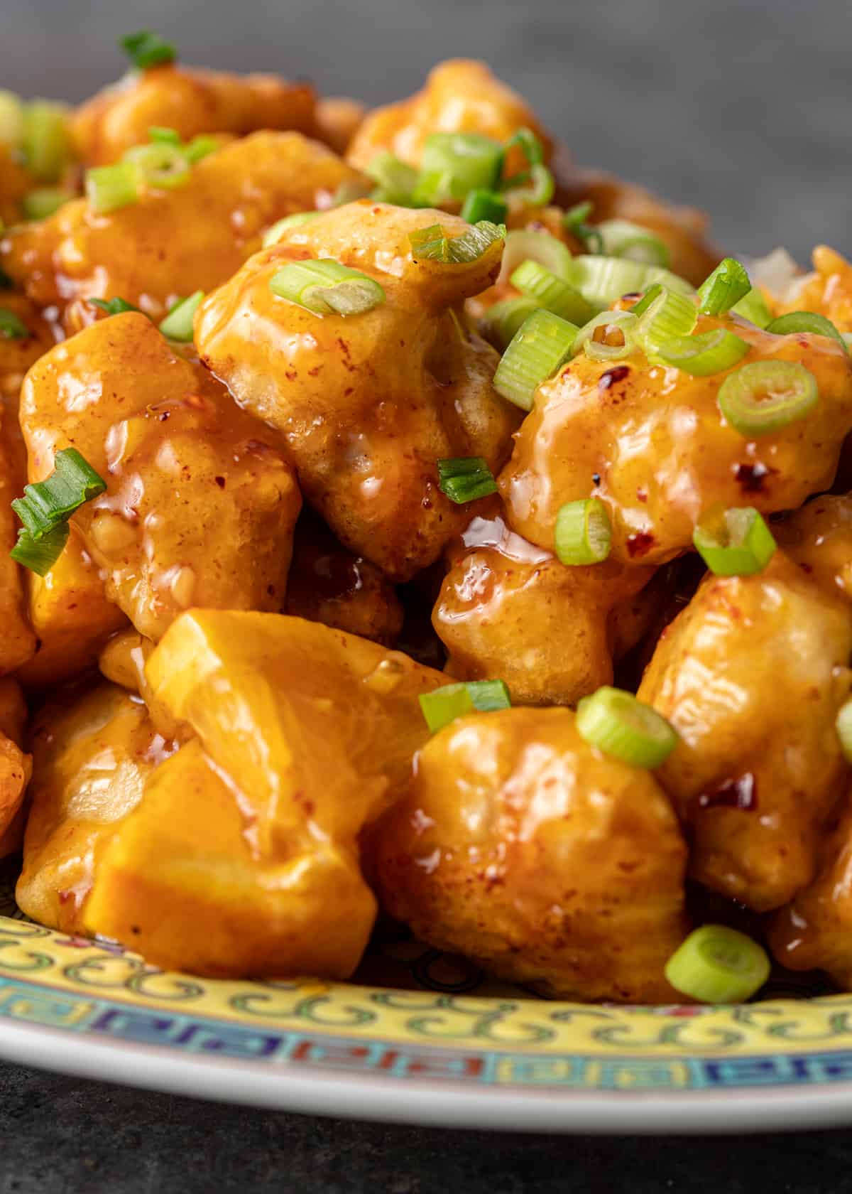 extreme closeup: orange chicken on a ceramic plate with sticky sauce and sliced green onions