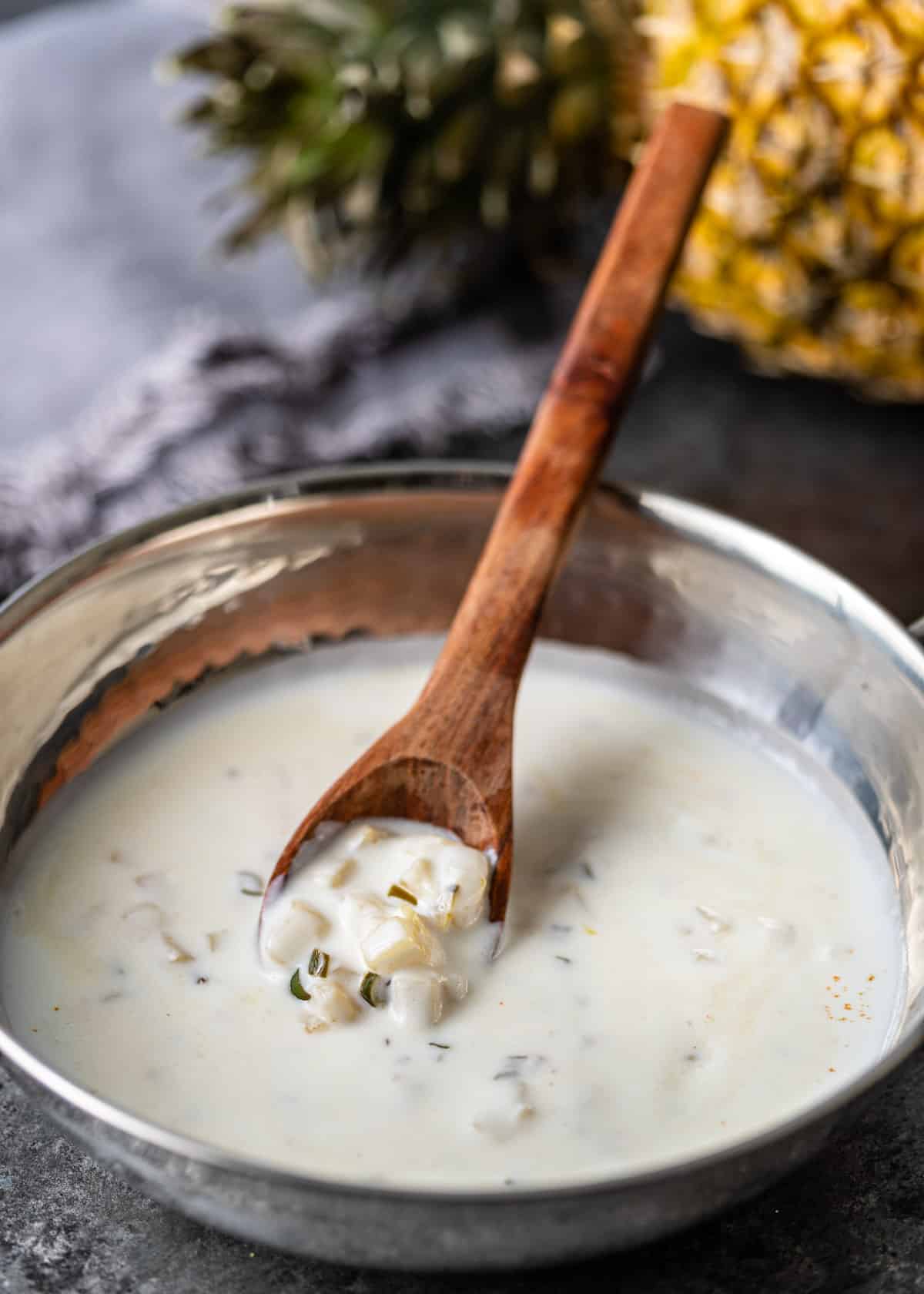 a metal pan full of pineapple raita with a wooden spoon