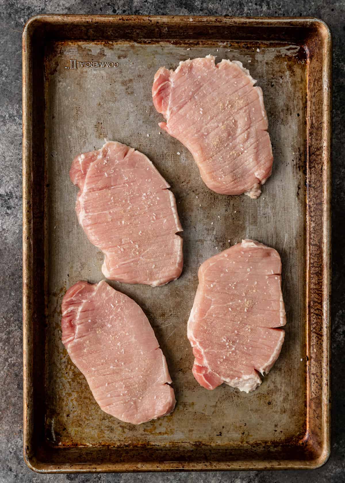 overhead: 4 seasoned and tenderized pork cutlets on a baking sheet