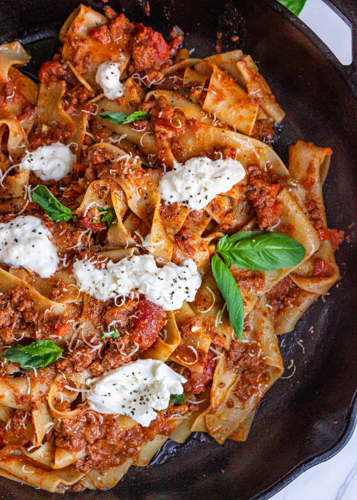 overhead: my bolognese sauce recipe with large noodles, burrata, and fresh basil on top