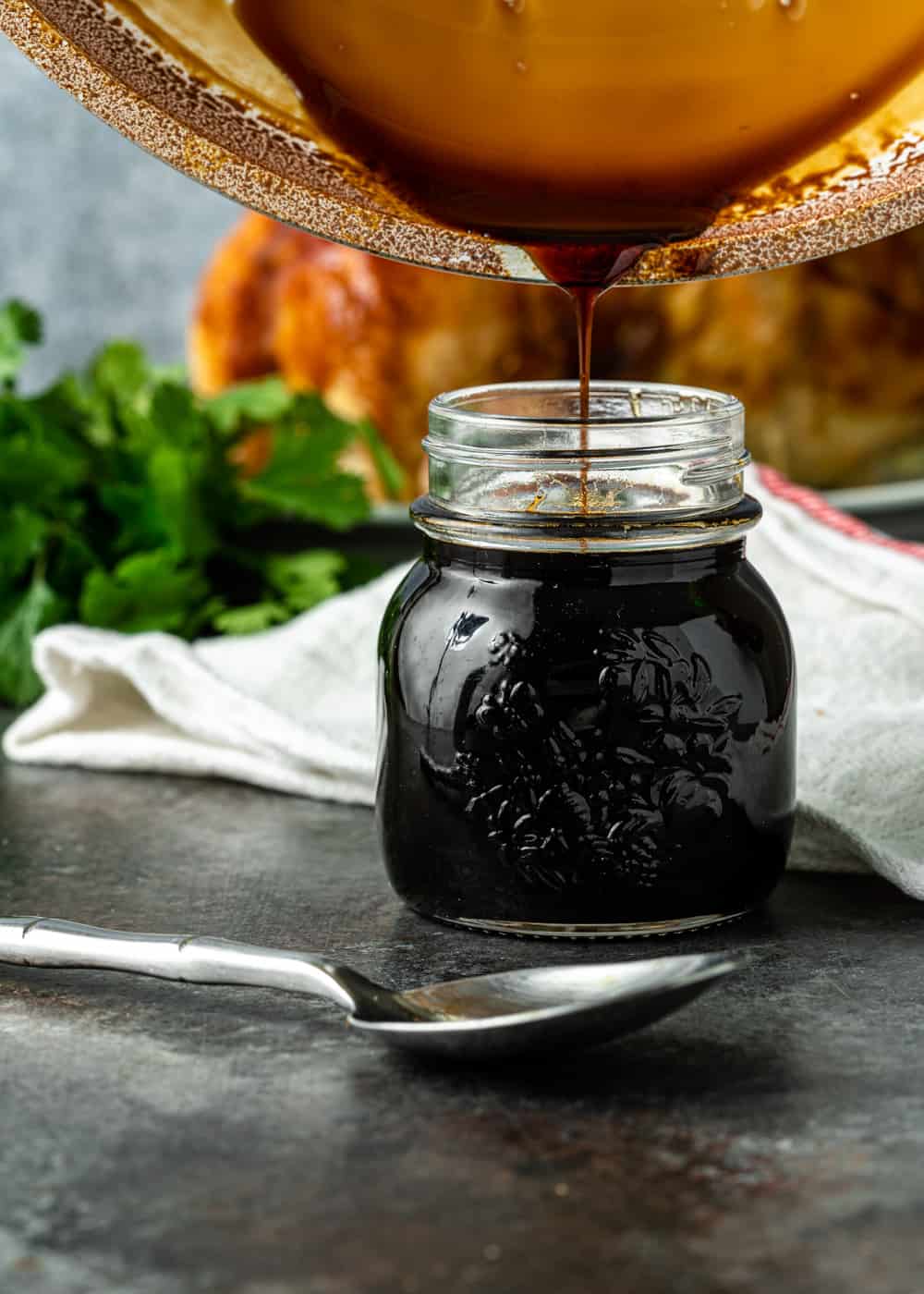 side view: pouring my teriyaki sauce recipe into a glass jar with a spoon in front of the jar