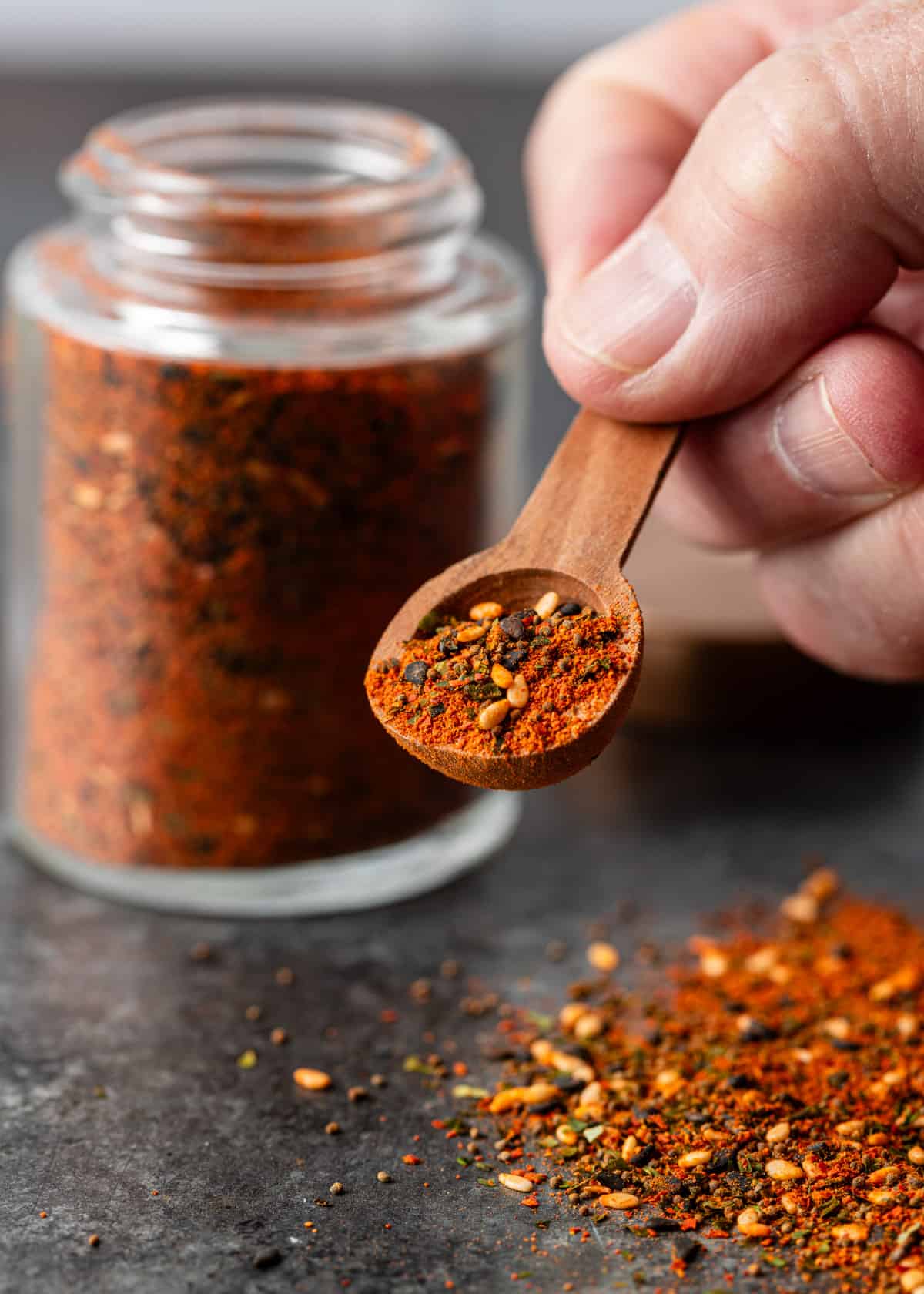 a hand lifting a small wooden spoon of shichimi togarashi