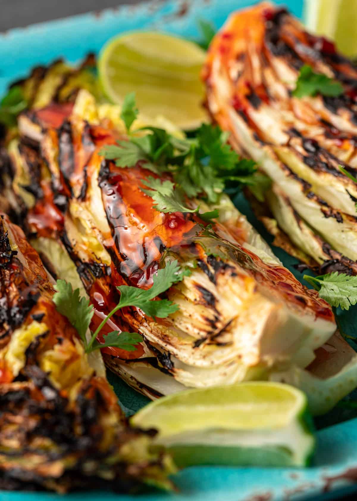 extreme closeup: charred cabbage with sweet chili sauce, fresh herbs, and a lime slice