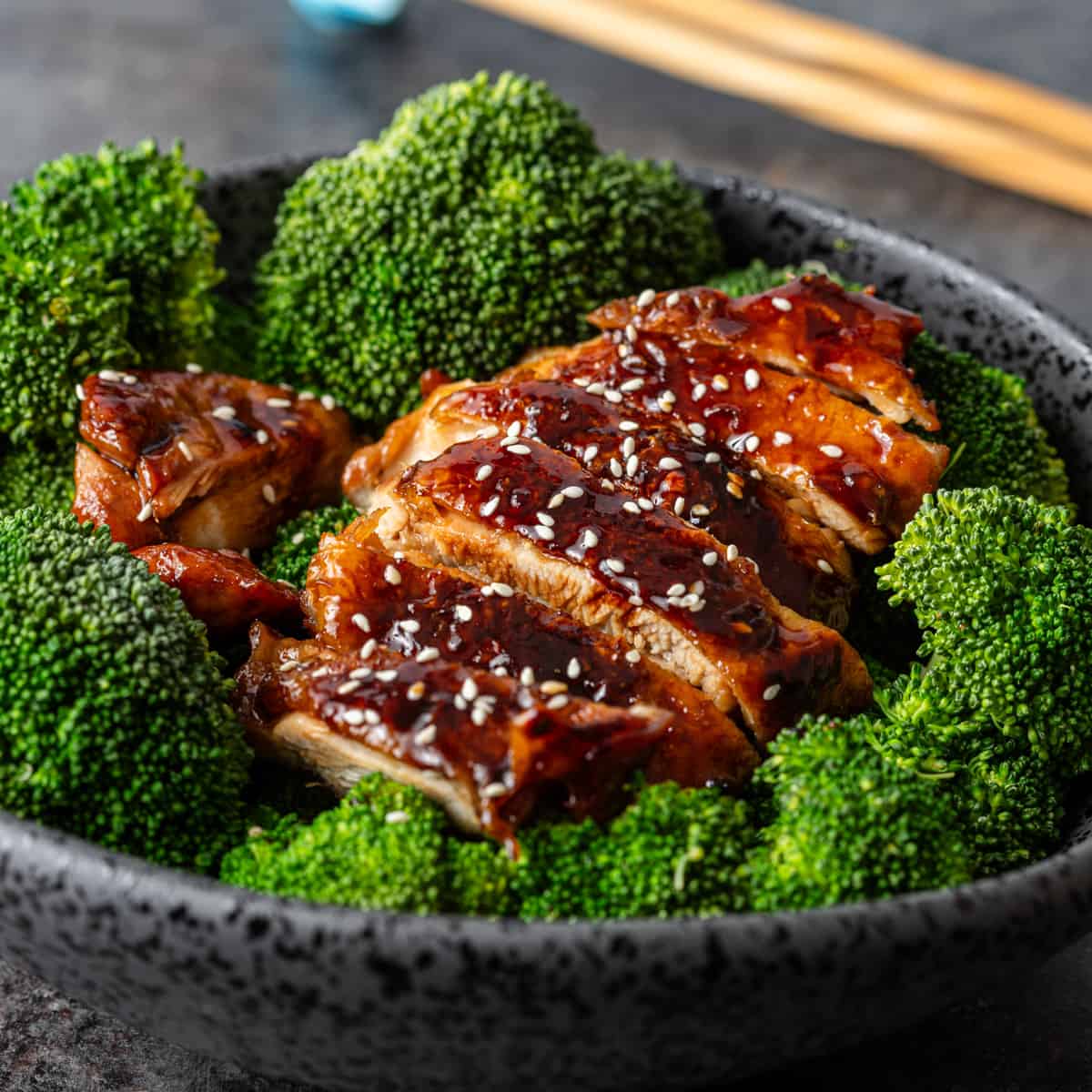 closeup: teriyaki chicken over cooked broccoli in a black bowl