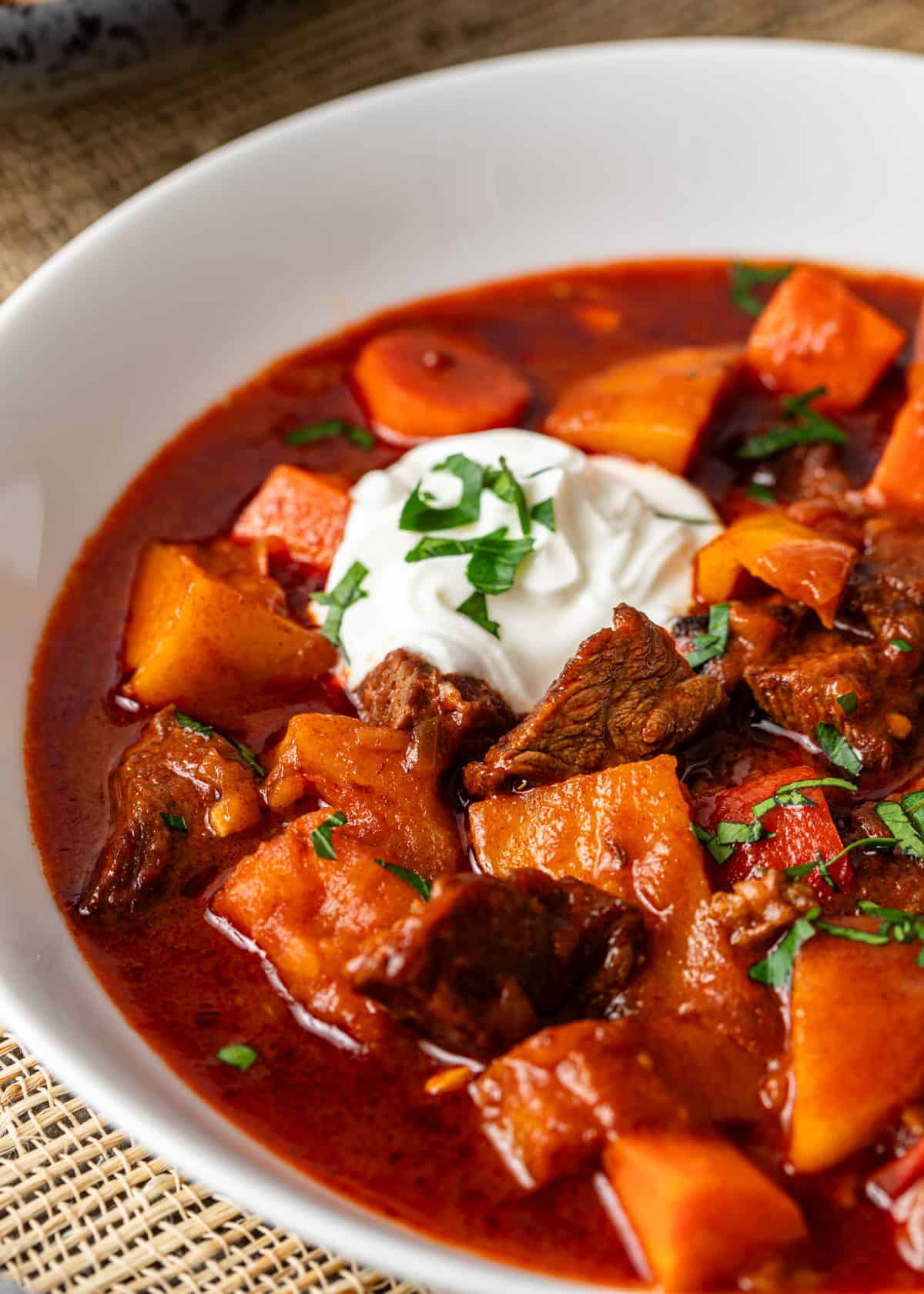 extreme closeup: hungarian goulash in a bowl with sour creamw, beef, and vegetables showing
