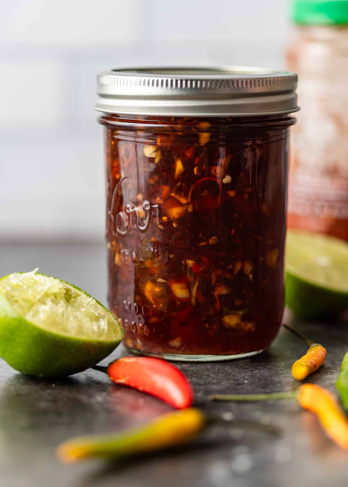 a mason jar full of vietnamese dipping sauce with lime and peppers to the side