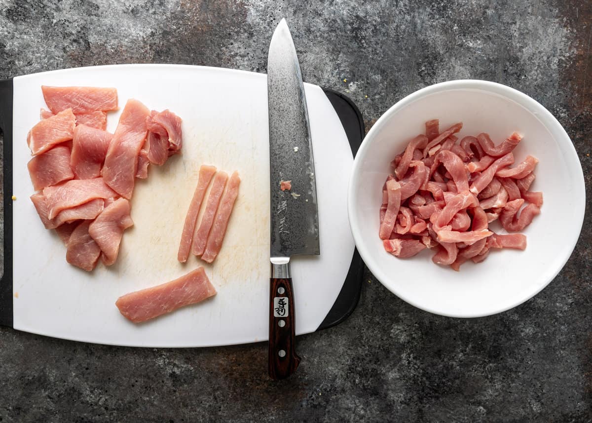 overhead: slicing pork on a white cutting board for vinegar pork stir fry
